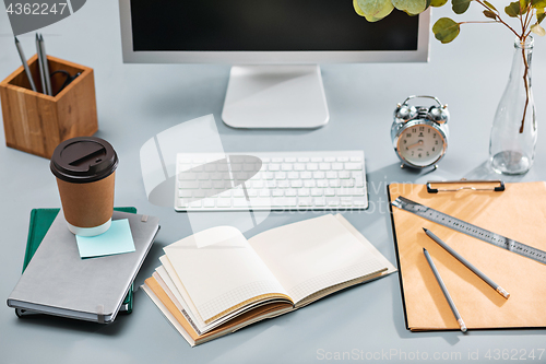 Image of The gray desk with laptop, notepad with blank sheet, pot of flower, stylus and tablet for retouching