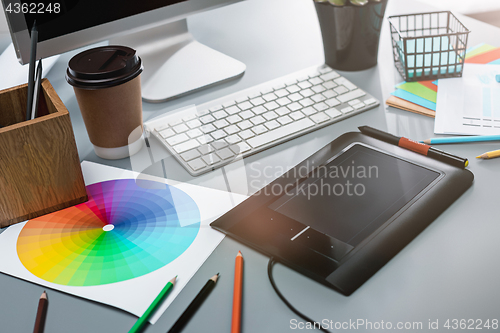 Image of The gray desk with laptop, notepad with blank sheet, pot of flower, stylus and tablet for retouching