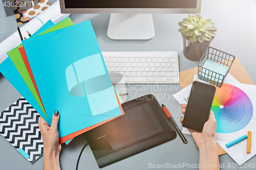 Image of The gray desk with laptop, notepad with blank sheet, pot of flower, stylus and tablet for retouching