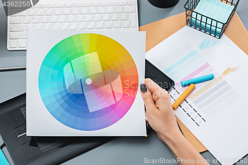 Image of The gray desk with laptop, notepad with blank sheet, pot of flower, stylus and tablet for retouching