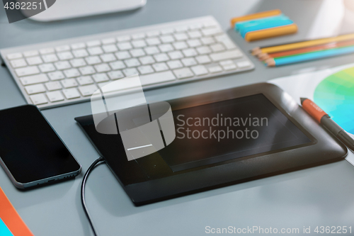 Image of The gray desk with laptop, notepad with blank sheet, pot of flower, stylus and tablet for retouching