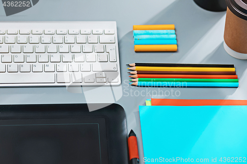 Image of The gray desk with laptop, notepad with blank sheet, pot of flower, stylus and tablet for retouching