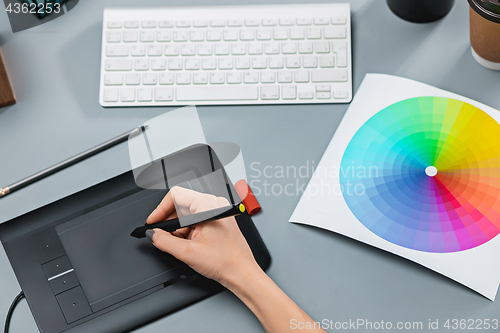 Image of The gray desk with laptop, notepad with blank sheet, pot of flower, stylus and tablet for retouching