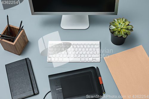 Image of The gray desk with laptop, notepad with blank sheet, pot of flower, stylus and tablet for retouching