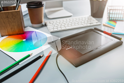 Image of The gray desk with laptop, notepad with blank sheet, pot of flower, stylus and tablet for retouching