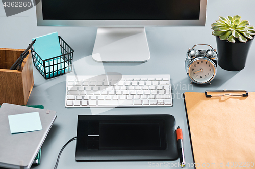 Image of The gray desk with laptop, notepad with blank sheet, pot of flower, stylus and tablet for retouching