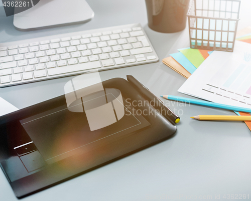 Image of The gray desk with laptop, notepad with blank sheet, pot of flower, stylus and tablet for retouching