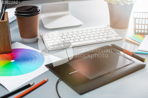 Image of The gray desk with laptop, notepad with blank sheet, pot of flower, stylus and tablet for retouching