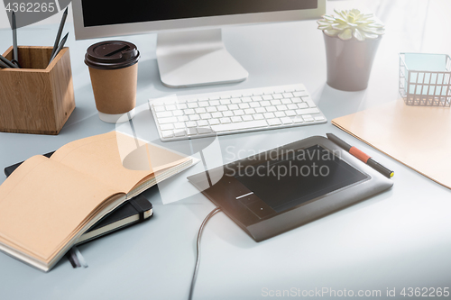 Image of The gray desk with laptop, notepad with blank sheet, pot of flower, stylus and tablet for retouching