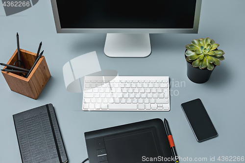 Image of The gray desk with laptop, notepad with blank sheet, pot of flower, stylus and tablet for retouching