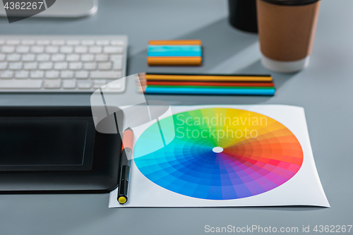 Image of The gray desk with laptop, notepad with blank sheet, pot of flower, stylus and tablet for retouching