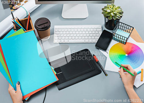 Image of The gray desk with laptop, notepad with blank sheet, pot of flower, stylus and tablet for retouching