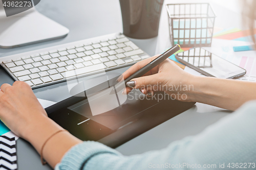 Image of The gray desk with laptop, notepad with blank sheet, pot of flower, stylus and tablet for retouching