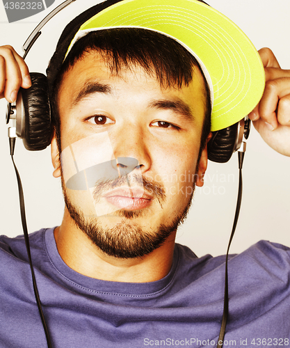 Image of young asian man in hat and headphones listening music on white b