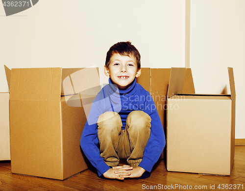 Image of little cute boy in empty room, remoove to new house. home alone emong boxes close up kid smiling