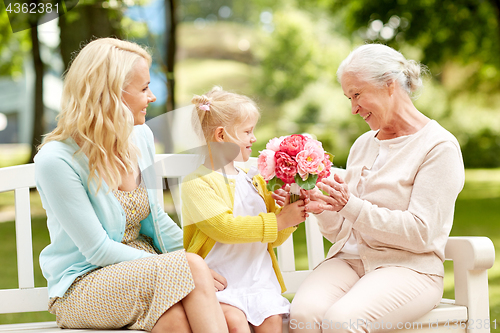 Image of happy family giving flowers to grandmother at park