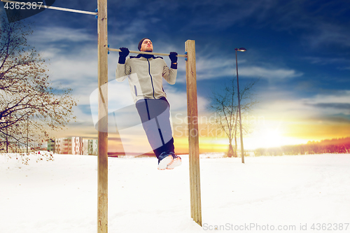 Image of young man exercising on horizontal bar in winter