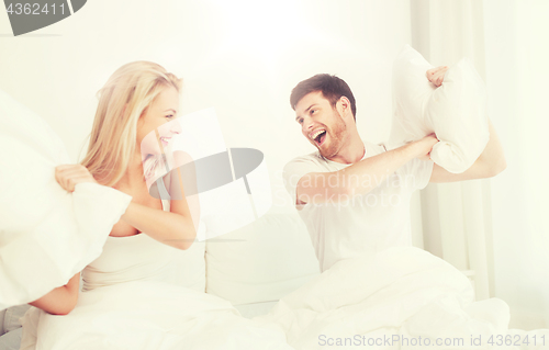 Image of happy couple having pillow fight in bed at home