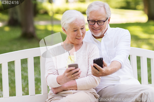 Image of happy senior couple with smartphones at park