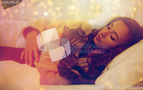 Image of happy young woman with cat lying in bed at home