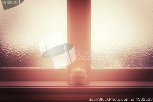 Image of Frosted window and burning candle and in misty light