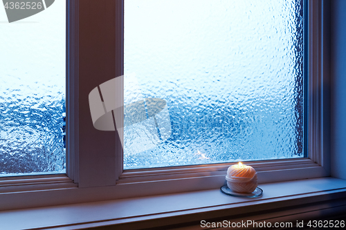 Image of Cozy candle burning near a frosted window