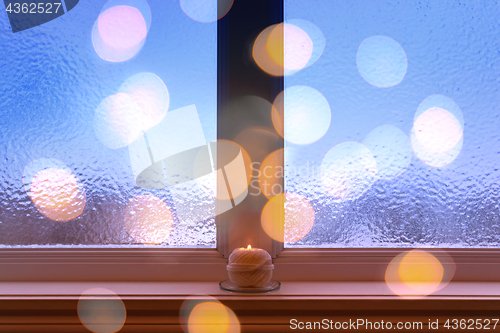 Image of Frosted window, burning candle and bokeh lights