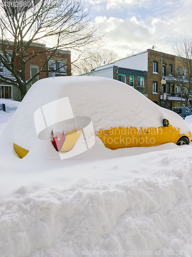 Image of Urban street with a yellow car stuck in snow