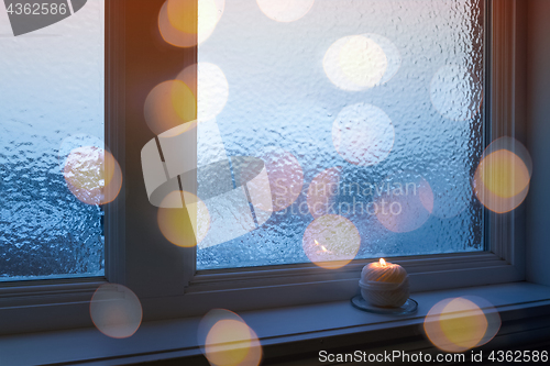 Image of Frosted window, candle and golden bokeh lights