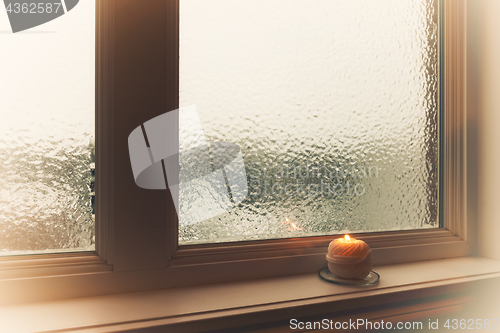 Image of Burning candle and frosted window in hazy light