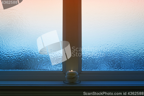 Image of Frosted evening window with a candle burning