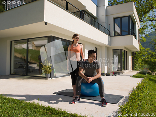 Image of woman and personal trainer doing exercise with pilates ball