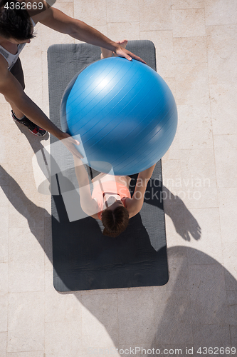Image of woman and personal trainer doing exercise with pilates ball