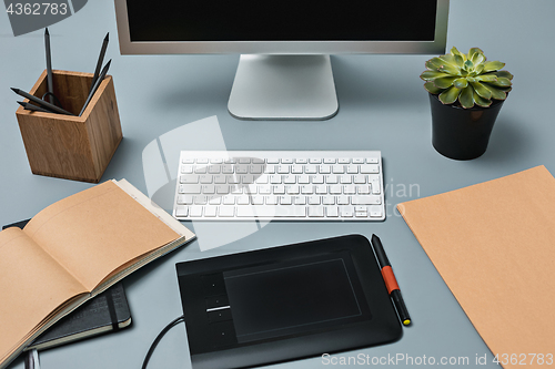 Image of The gray desk with laptop, notepad with blank sheet, pot of flower, stylus and tablet for retouching