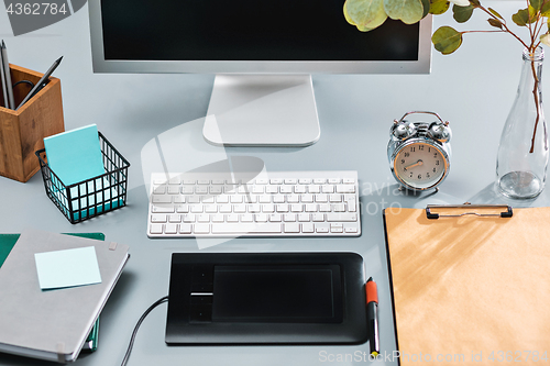 Image of The gray desk with laptop, notepad with blank sheet, pot of flower, stylus and tablet for retouching