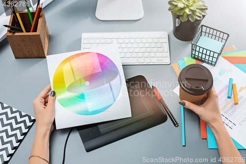 Image of The gray desk with laptop, notepad with blank sheet, pot of flower, stylus and tablet for retouching