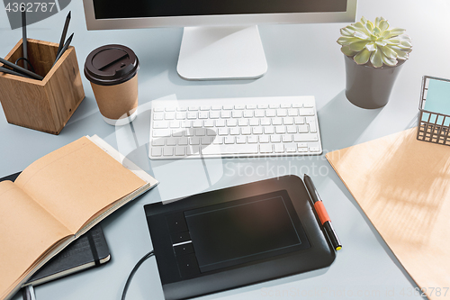 Image of The gray desk with laptop, notepad with blank sheet, pot of flower, stylus and tablet for retouching