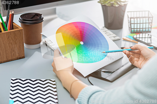 Image of The gray desk with laptop, notepad with blank sheet, pot of flower, stylus and tablet for retouching