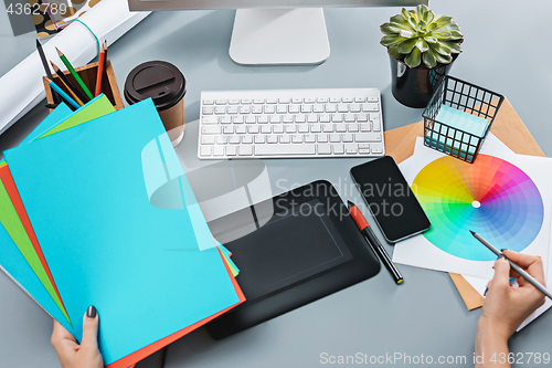 Image of The gray desk with laptop, notepad with blank sheet, pot of flower, stylus and tablet for retouching