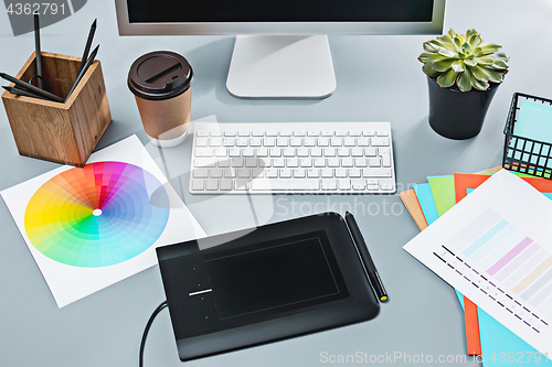 Image of The gray desk with laptop, notepad with blank sheet, pot of flower, stylus and tablet for retouching