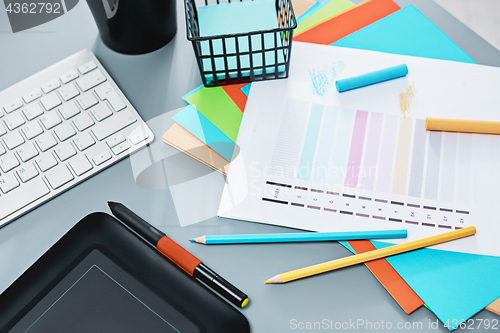 Image of The gray desk with laptop, notepad with blank sheet, pot of flower, stylus and tablet for retouching