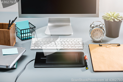 Image of The gray desk with laptop, notepad with blank sheet, pot of flower, stylus and tablet for retouching