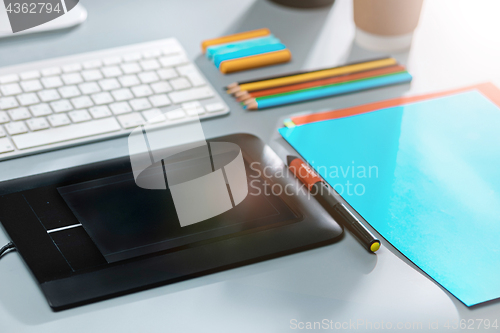 Image of The gray desk with laptop, notepad with blank sheet, pot of flower, stylus and tablet for retouching