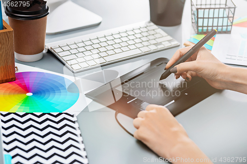 Image of The gray desk with laptop, notepad with blank sheet, pot of flower, stylus and tablet for retouching