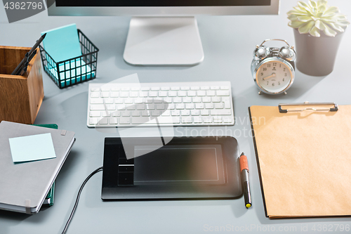 Image of The gray desk with laptop, notepad with blank sheet, pot of flower, stylus and tablet for retouching