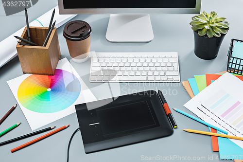 Image of The gray desk with laptop, notepad with blank sheet, pot of flower, stylus and tablet for retouching