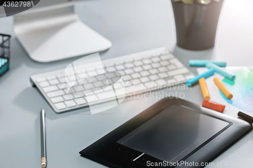 Image of The gray desk with laptop, notepad with blank sheet, pot of flower, stylus and tablet for retouching