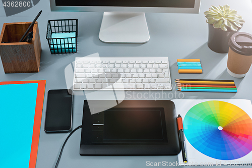 Image of The gray desk with laptop, notepad with blank sheet, pot of flower, stylus and tablet for retouching