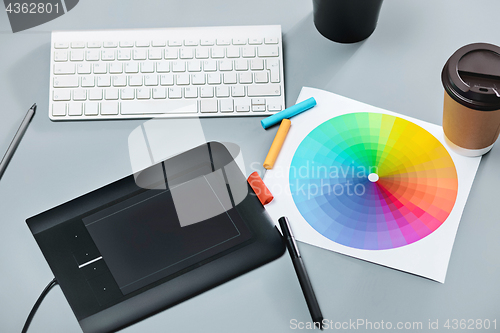 Image of The gray desk with laptop, notepad with blank sheet, pot of flower, stylus and tablet for retouching