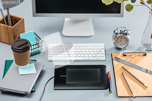 Image of The gray desk with laptop, notepad with blank sheet, pot of flower, stylus and tablet for retouching